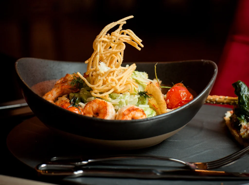 Shrimp Caesar salad topped with potato shoestrings, prepared tableside